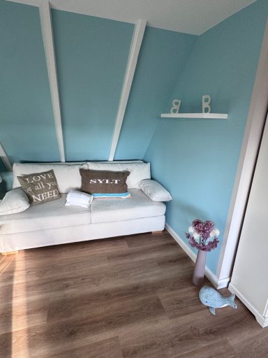 Heller Raum mit blauem Anstrich, weißem Sofa und einem kleinen Regal an der Wand.